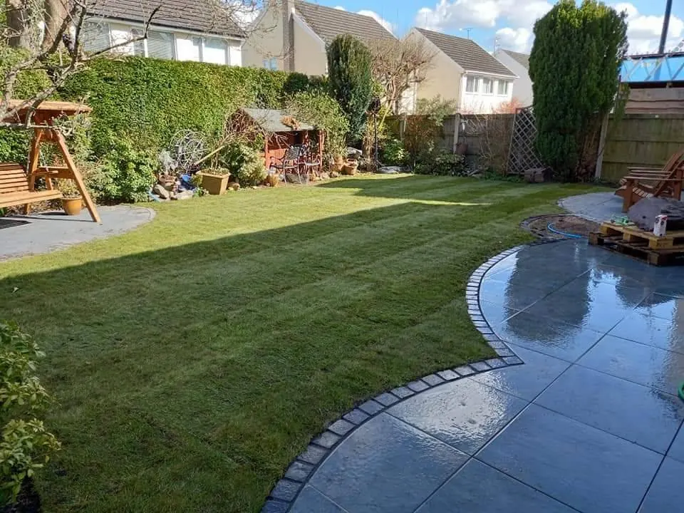 A grey porcelain path curving around a newly laid lawn, with a timber swing seat and hedging beyond