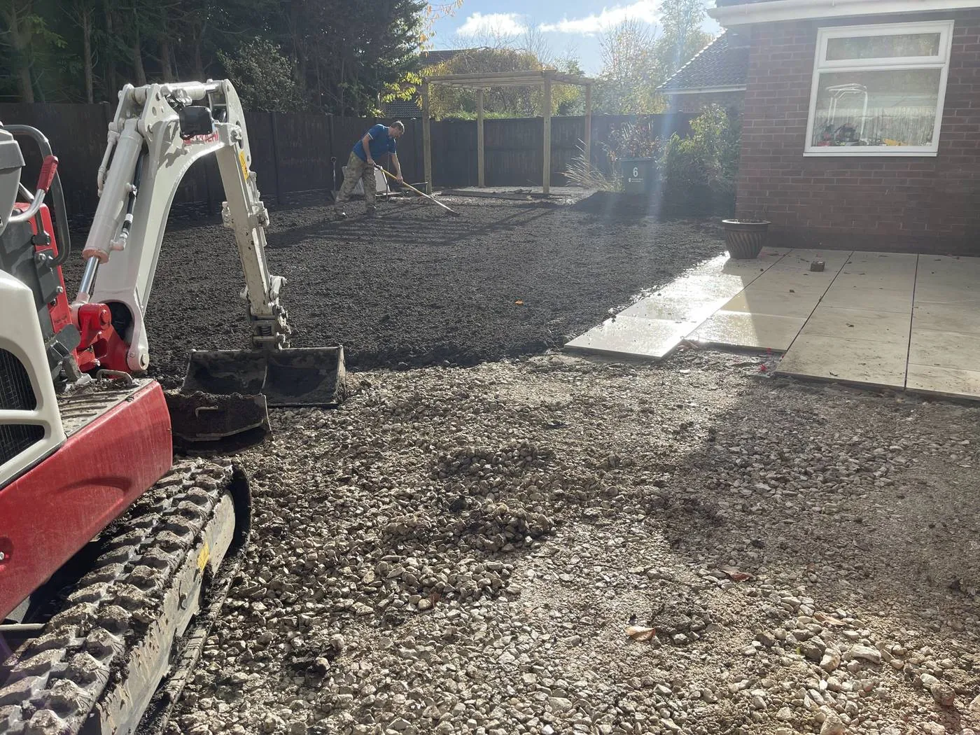 A micro excavator setting levels across a cleared garden beside newly laid paving