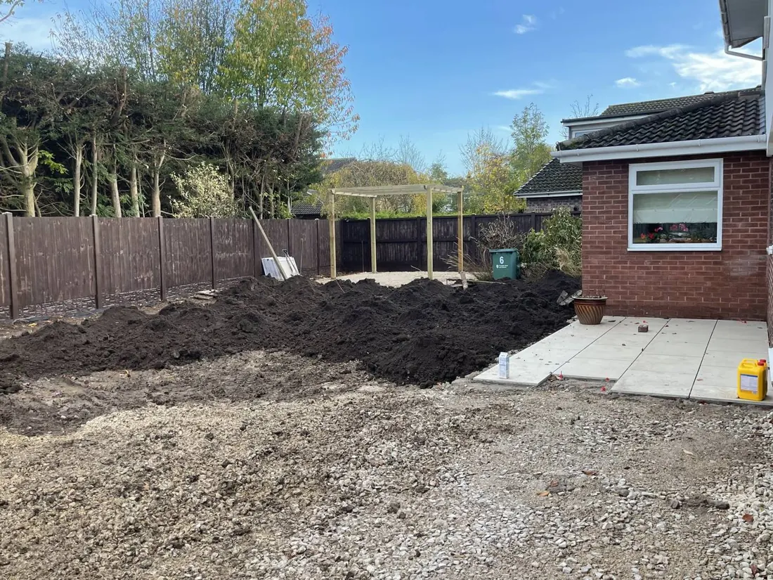 A back garden stripped back to bare soil beside a brick house