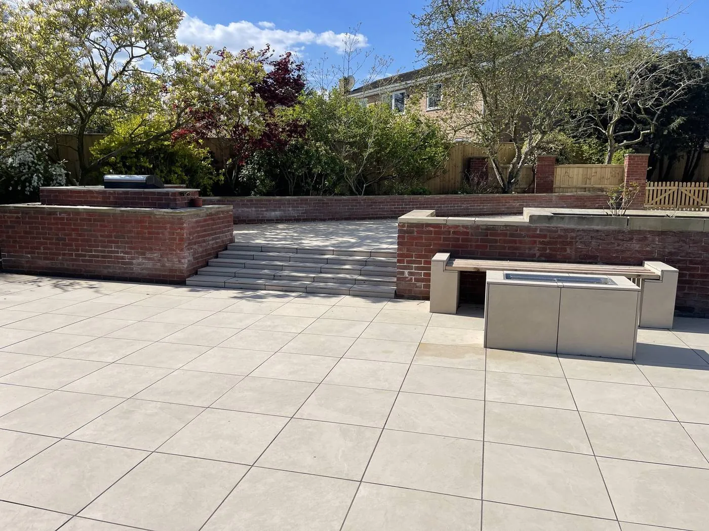 A pale porcelain terrace with brick retaining walls, wide steps and a built-in fire table